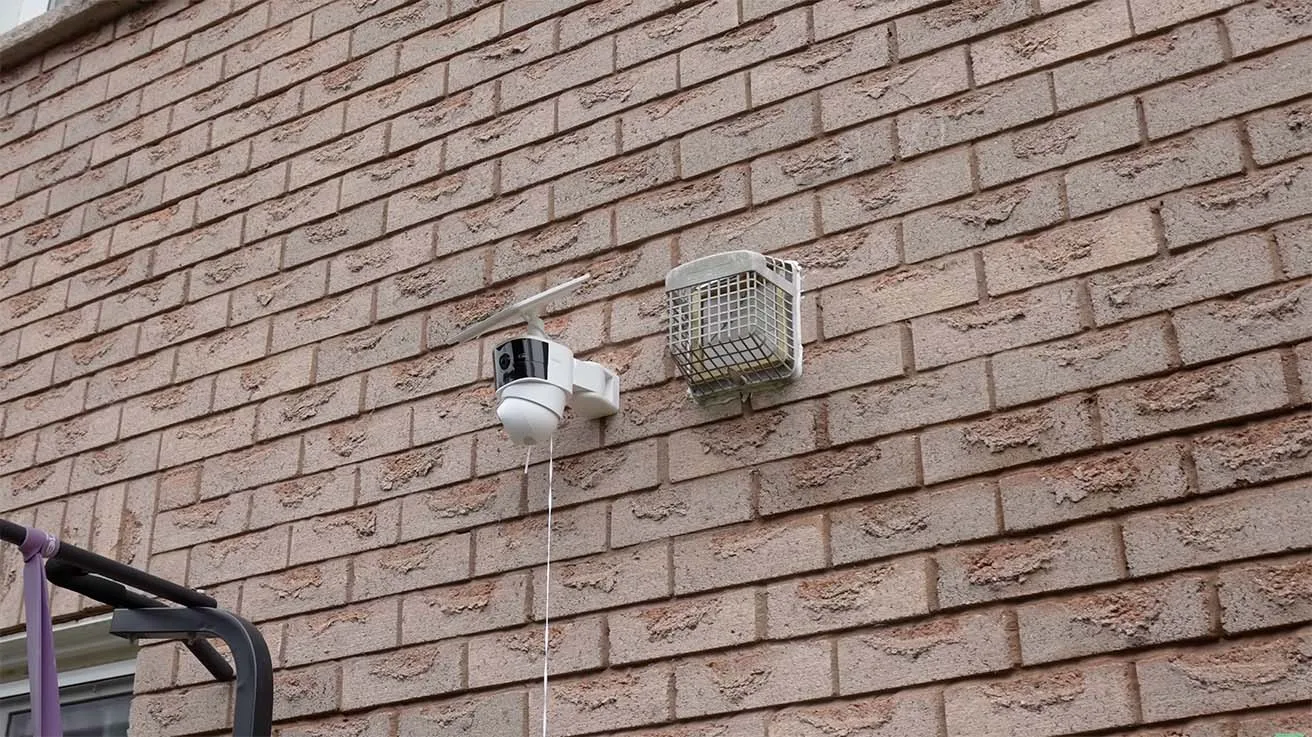 Existing outdoor security camera with a solar panel mounted on a brick wall beside an exterior vent