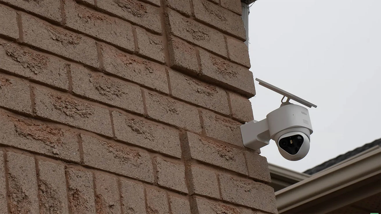 aosu outdoor security camera with a solar panel mounted at the corner of a brick house